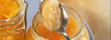 Ein Glas Melonen-Pfirsich-Marmelade auf einem Tisch, umgeben von Früchten.
