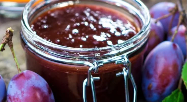 Selbstgemachte Zwetschgenmarmelade in einem Glas mit frischen Zwetschgen.